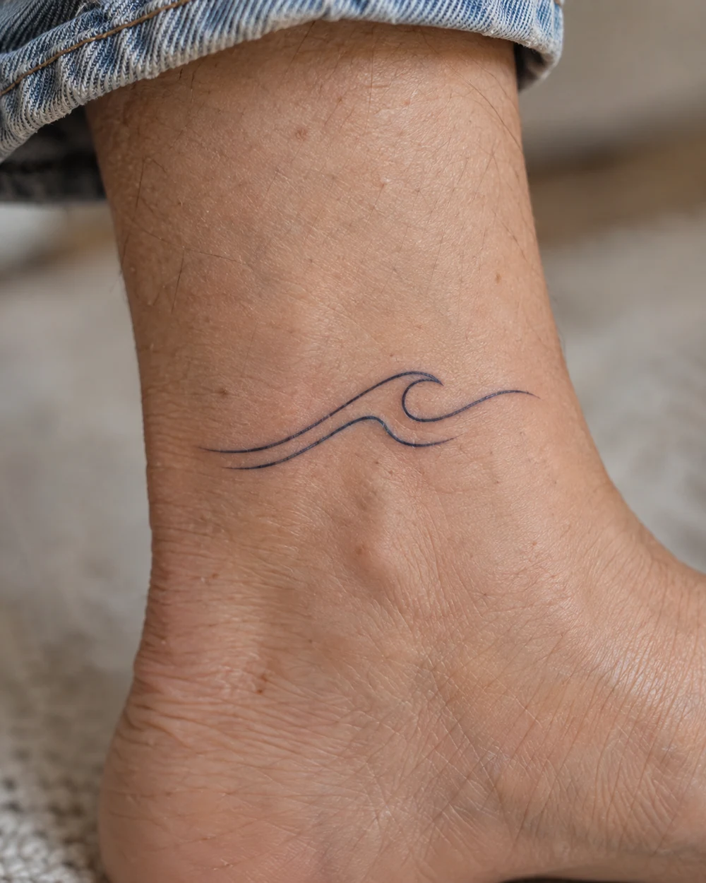Compact black two-line wave tattoo on the side of an ankle