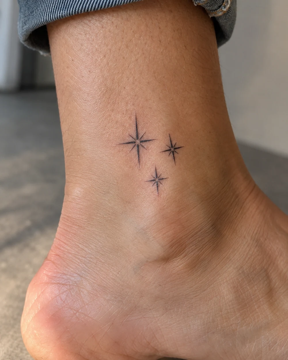 Three fine-line black star tattoos clustered above the ankle