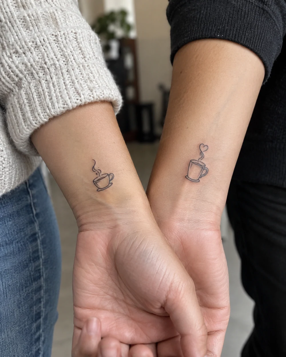 Matching fine-line coffee cup tattoos with different steam curls on two wrists