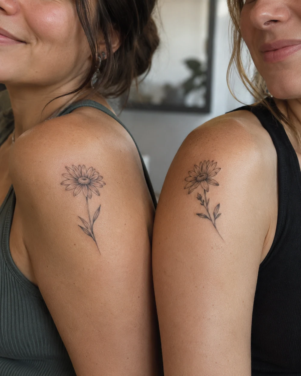 Matching fine-line daisy tattoos on two adult women’s shoulders