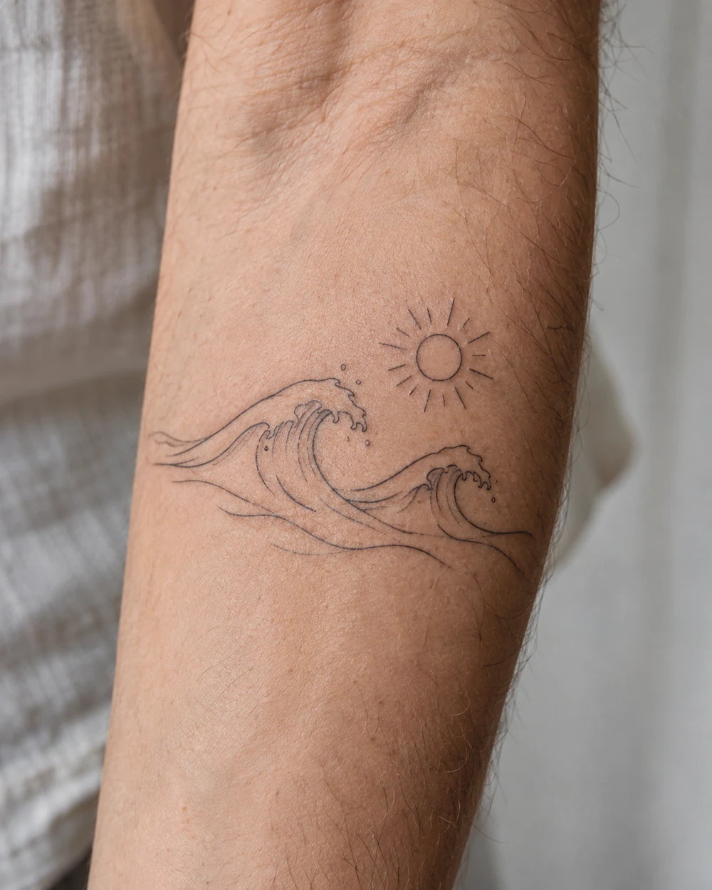 Minimal fine line tattoo of two flowing wave crests with an open sun above on a forearm