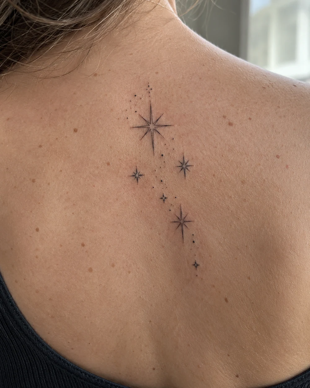 Fine line tattoo of five open stars with connecting dots on the upper back
