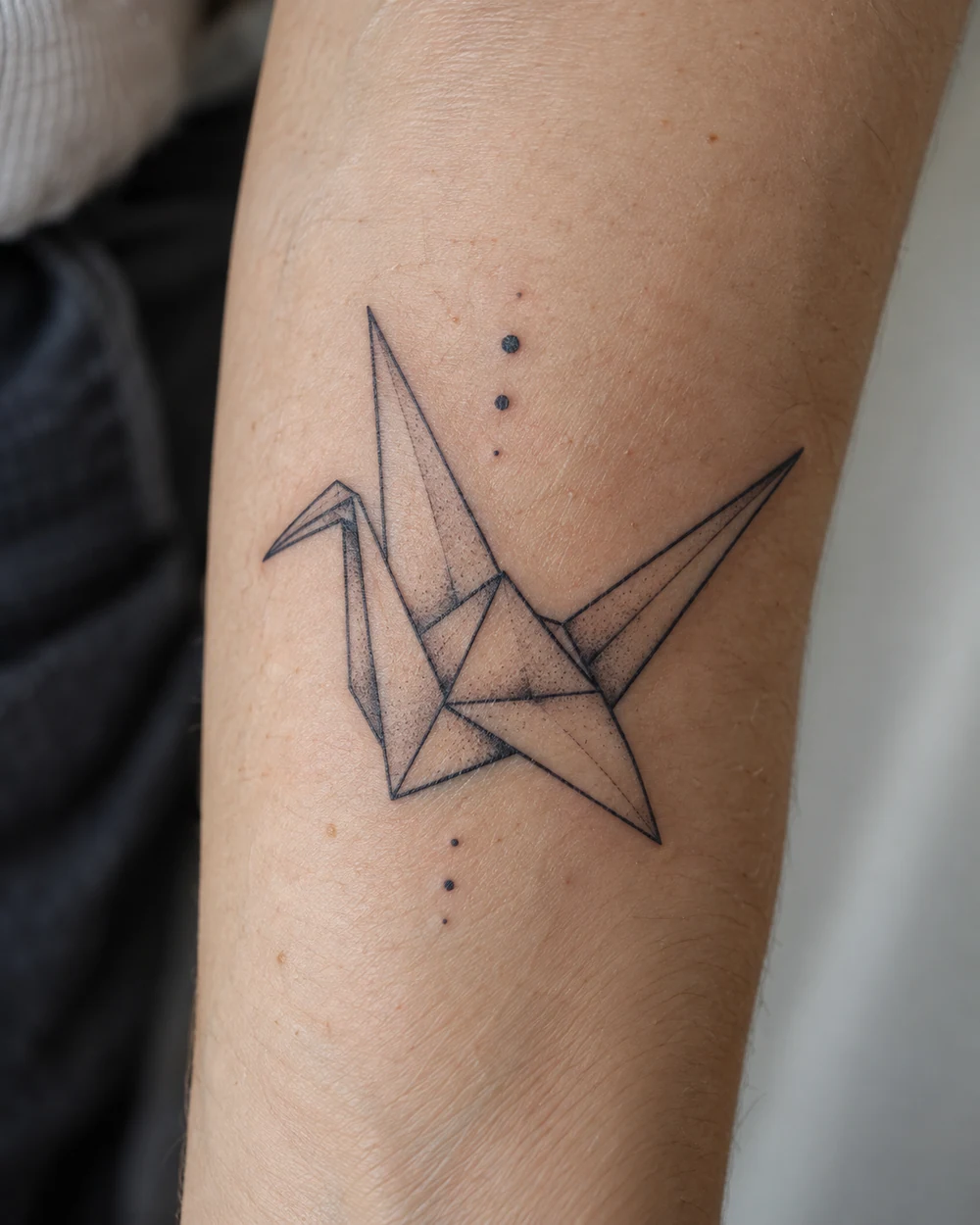 Fine-line geometric origami crane tattoo with small dot accents on a forearm