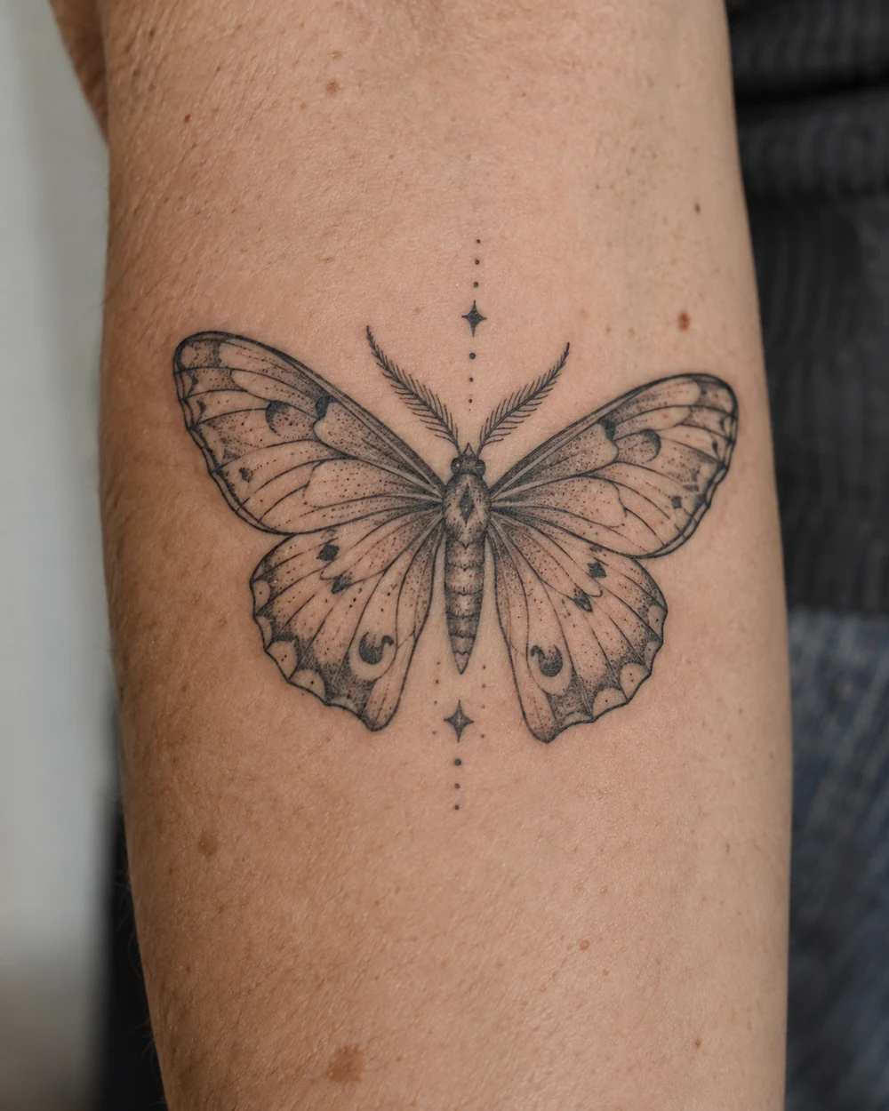 Symmetrical black moth with fine wing veins and surrounding dots forearm tattoo