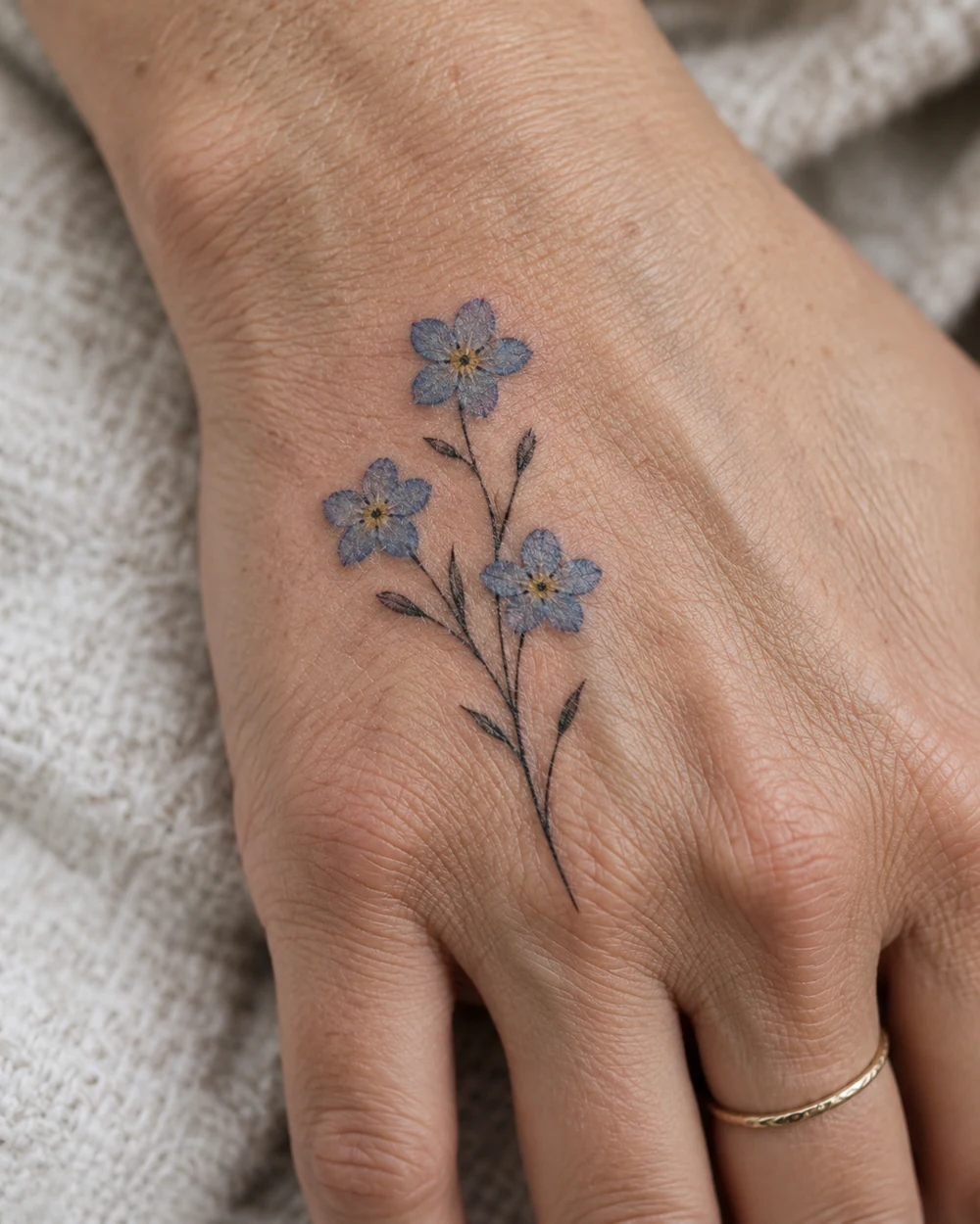 Blue forget-me-not flower tattoo with slender stems on the back of a hand
