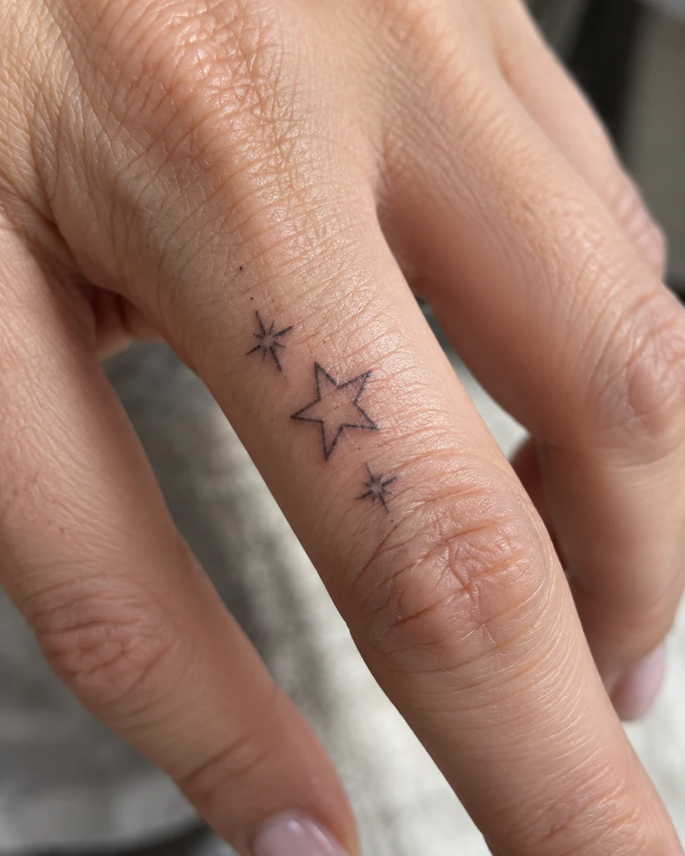 Outlined star and two sparkle tattoo beside a finger joint