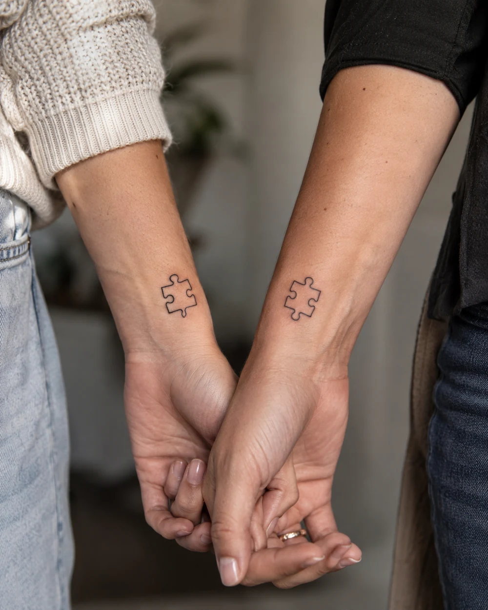 Two small black puzzle-piece tattoos on the wrists of hands held together