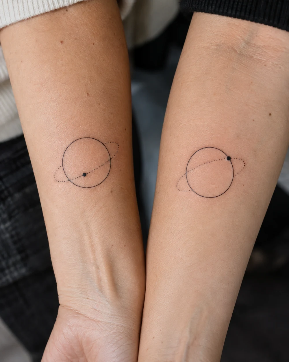 Matching fine-line circle and dotted orbit tattoos with differently positioned dots on two forearms