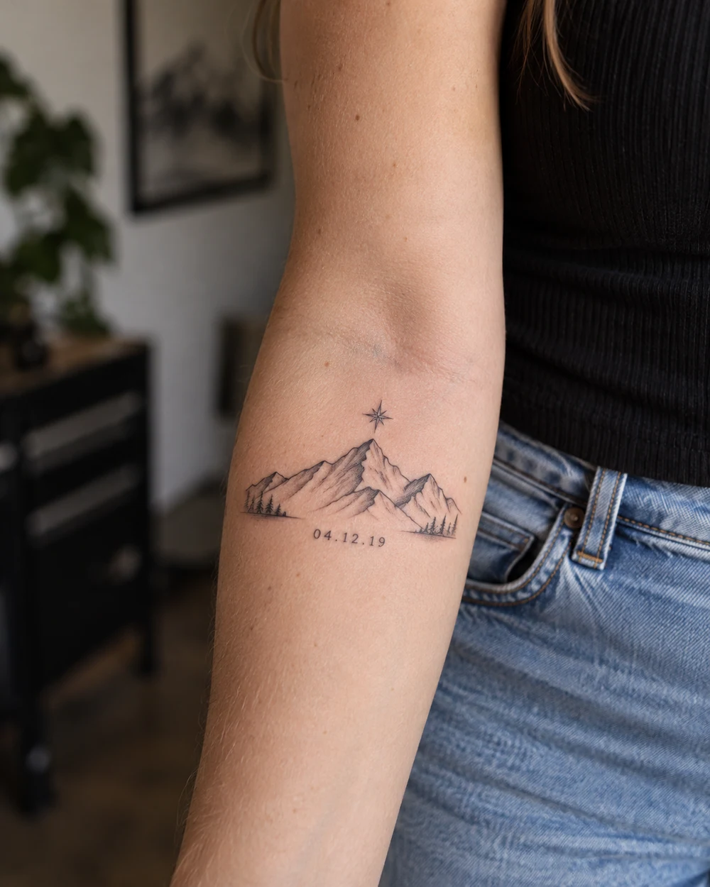 Fine-line mountain and star tattoo with a small date beneath on an outer forearm