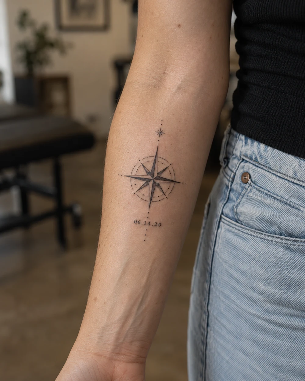Fine-line compass star tattoo with a date below on the forearm
