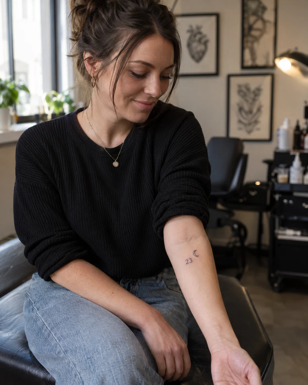 Small dark fine-line tattoo of a two-digit number and crescent moon on an inner forearm