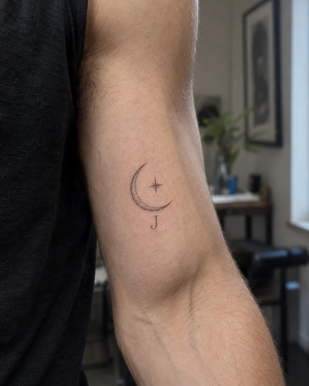 Fine-line crescent, tiny star, and initial memorial tattoo on an inner arm