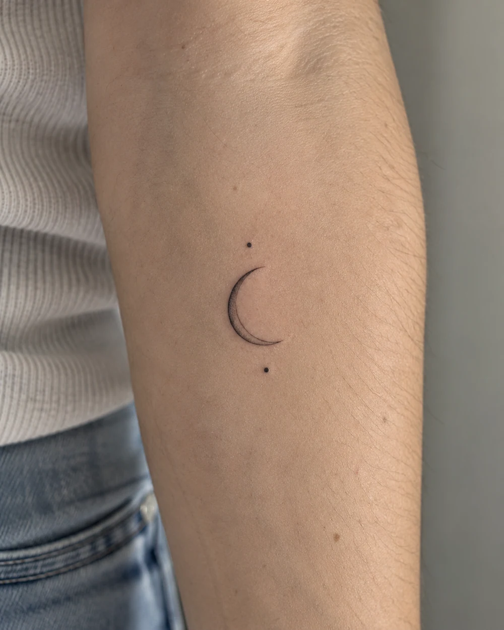 Thin black crescent moon tattoo with two separated dots on an inner forearm