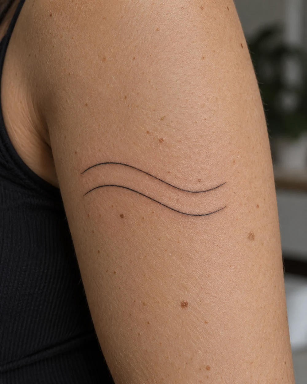 Two parallel, gently undulating fine-line black tattoo lines on an upper arm