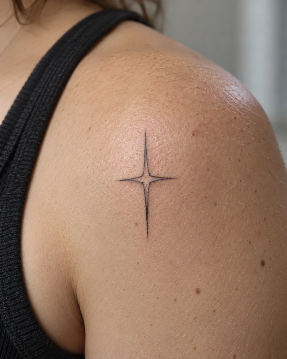 Fine-line four-point star tattoo on a shoulder