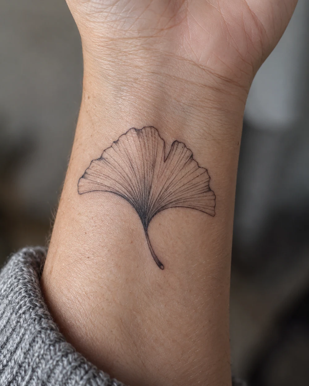 Fine-line black ginkgo leaf tattoo on an adult woman's inner wrist