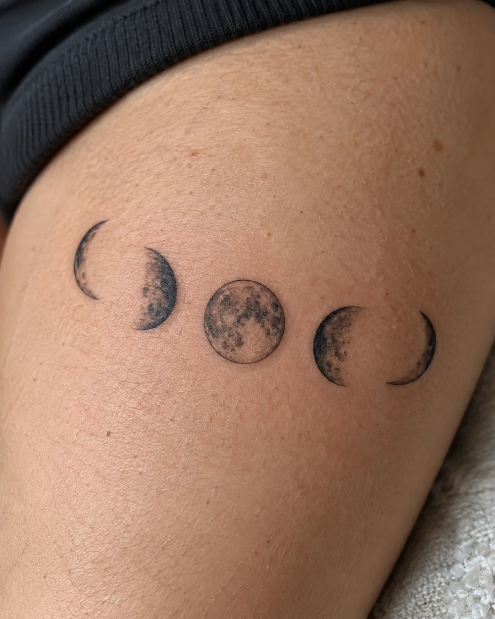 Five fine-line lunar phase tattoo shapes arranged in an arc on a forearm