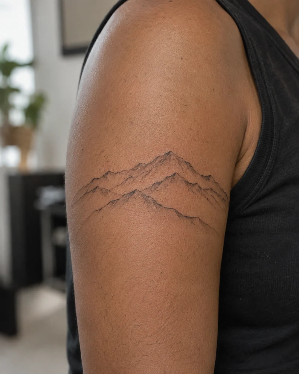 Fine-line mountain tattoo with overlapping ridges on an adult upper arm