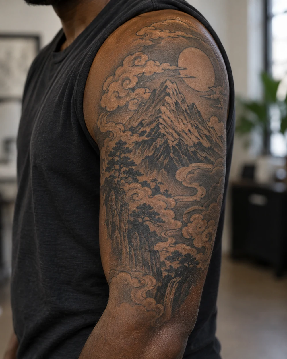 Black and gray Japanese-inspired mountain tattoo with flowing clouds covering an upper arm
