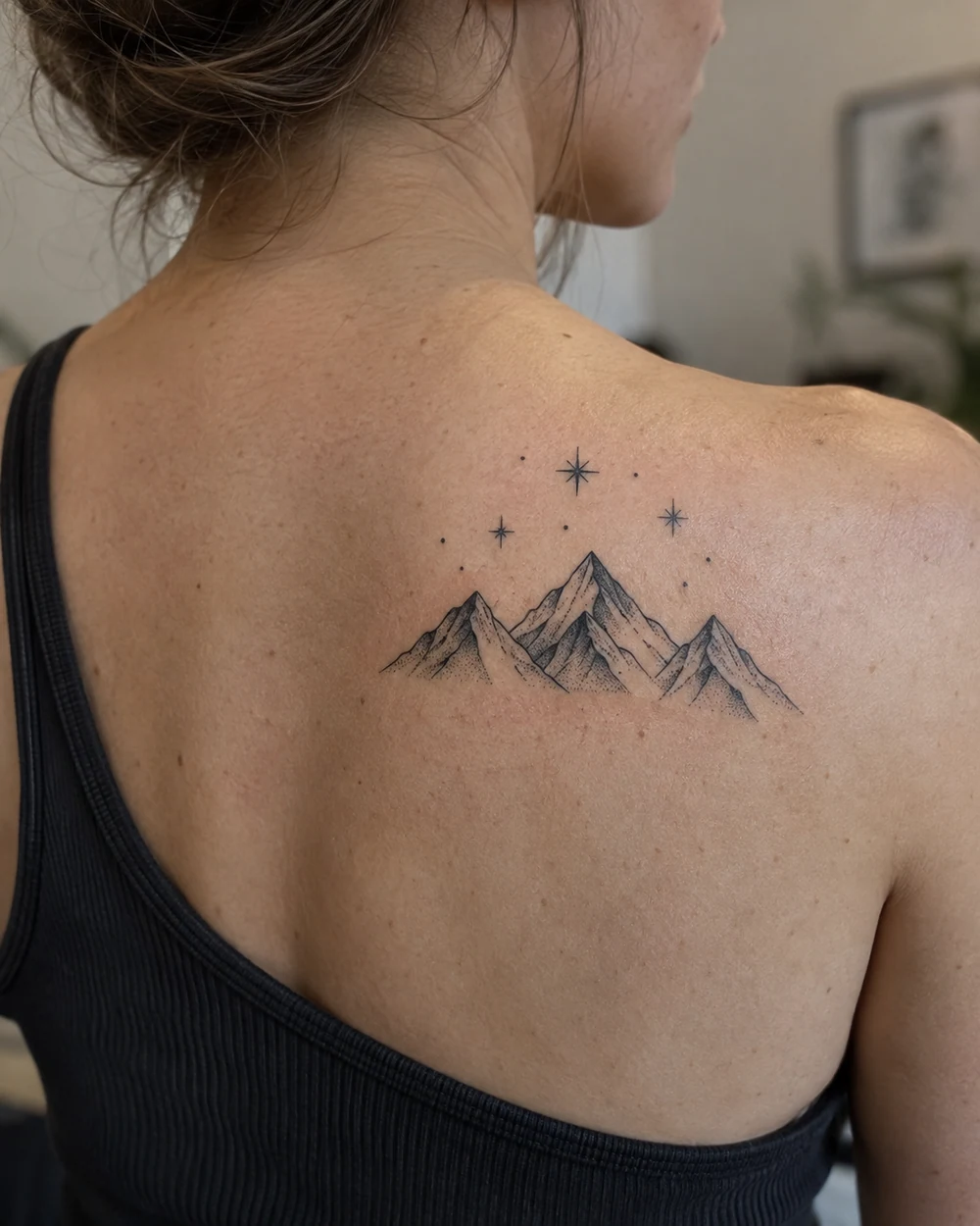 Black geometric mountain tattoo with scattered stars on a shoulder blade