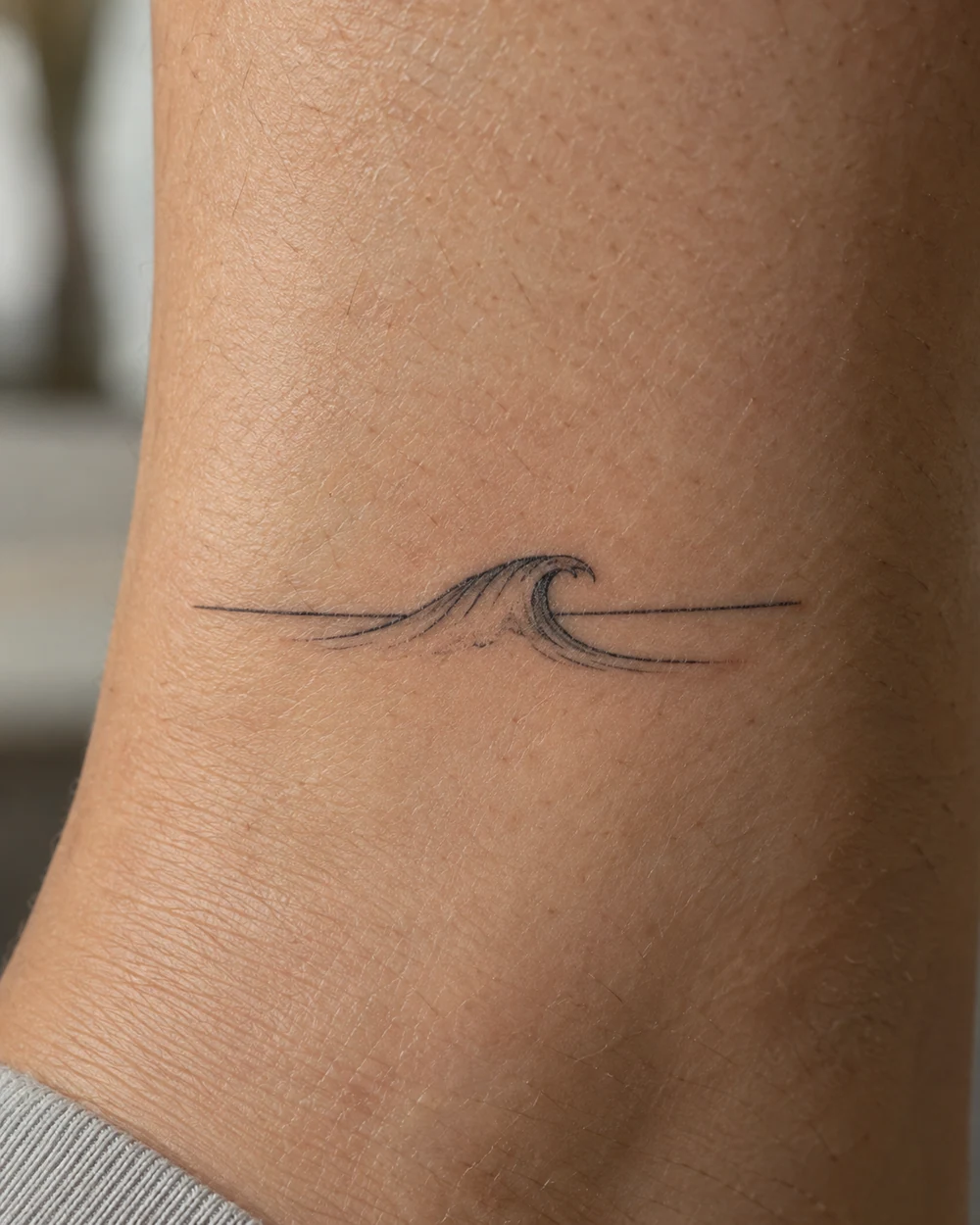 Minimalist black-line ocean wave tattoo beneath a straight horizon on skin