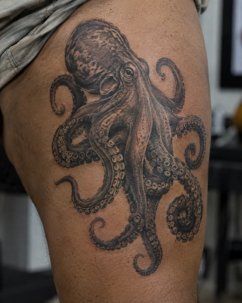 Realistic black-and-grey octopus tattoo with textured shading and detailed suckers on a thigh