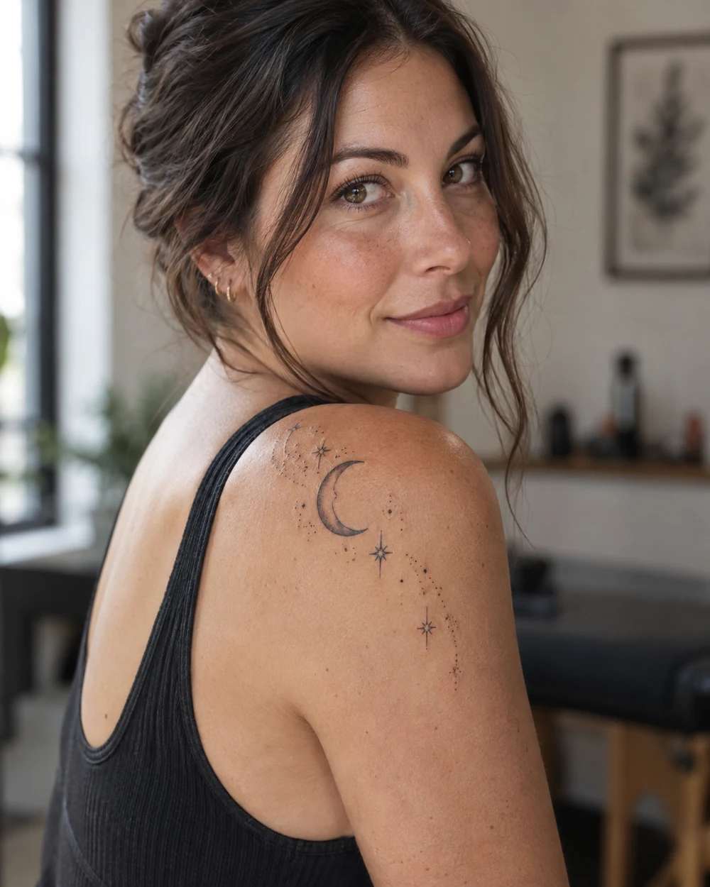 Fine-line crescent moon and stars tattoo arcing over a woman's shoulder