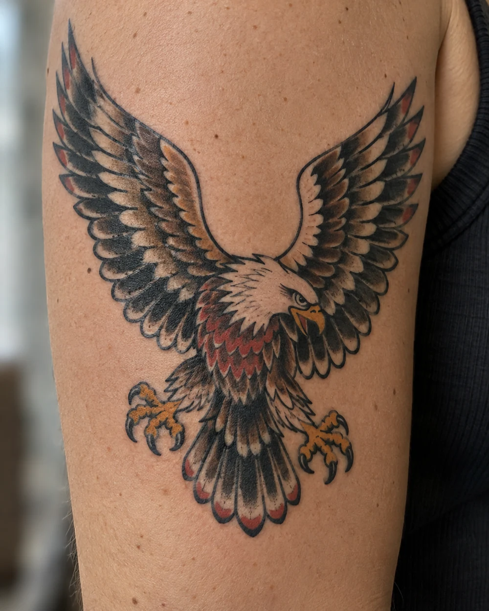 Traditional eagle tattoo with spread wings, cream and brown feathers, and red chest accents on an upper arm