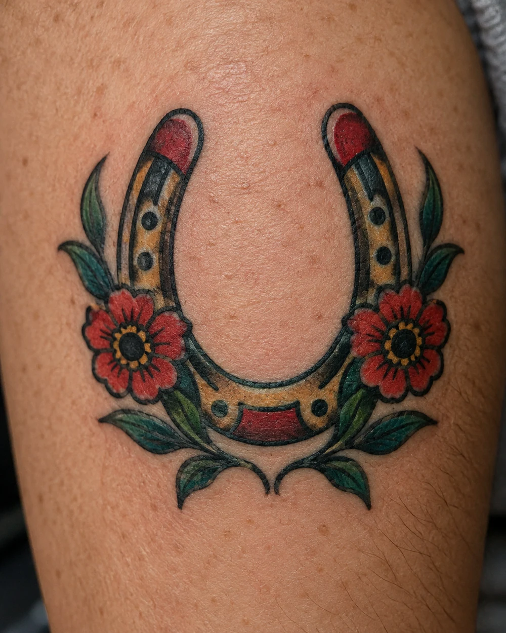 Traditional tattoo of an upright horseshoe framing two red flowers with curved green leaves
