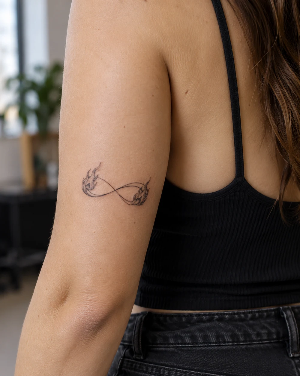 Two small black flames connected by an infinity loop tattoo on skin.