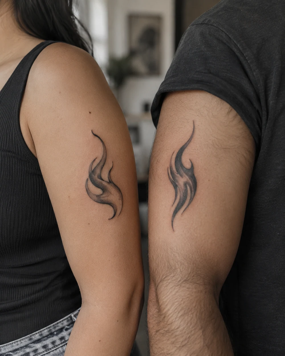 Asymmetrical black-and-gray flame tattoos on adjacent upper arms, one rounded and one pointed, facing inward.