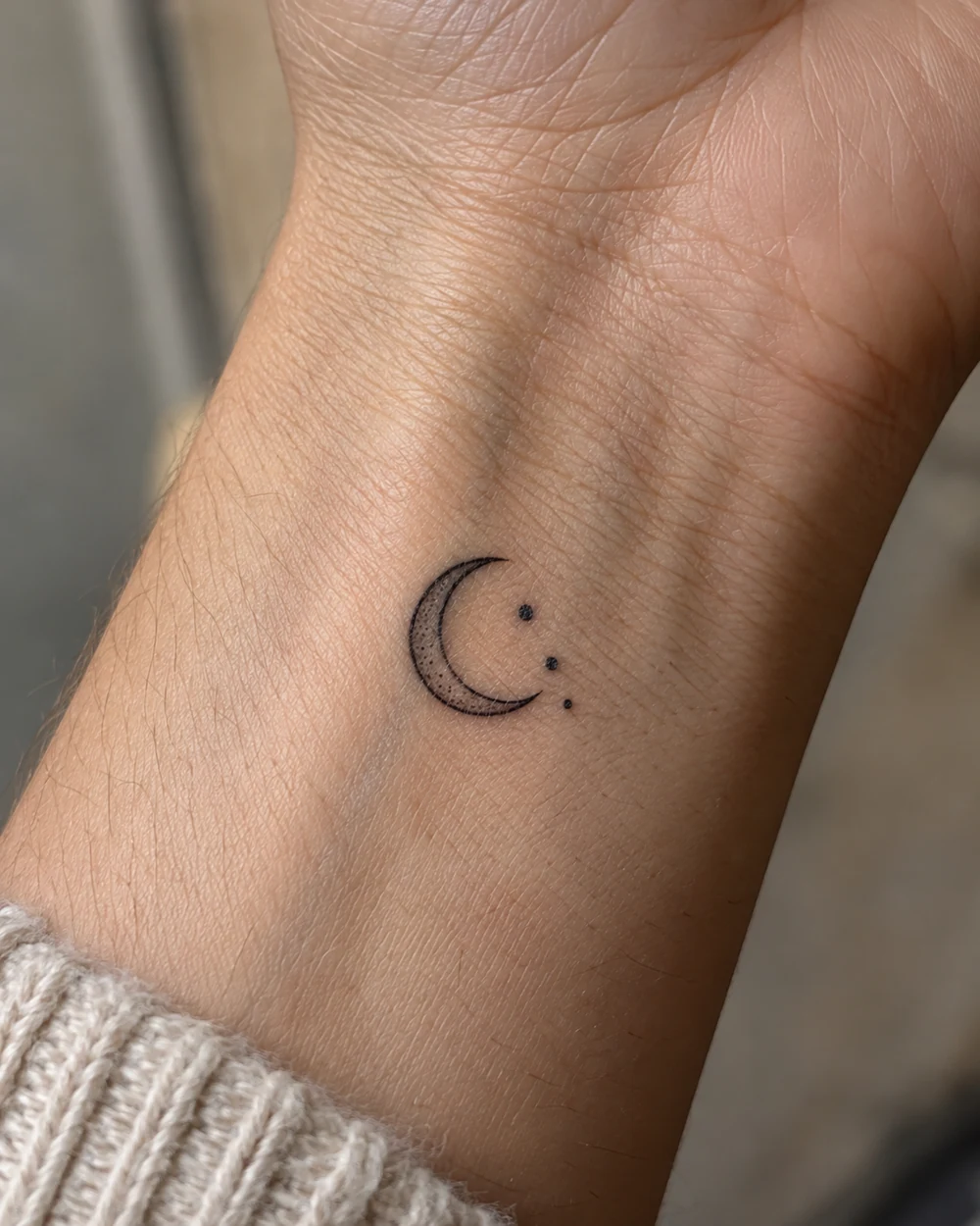 Tiny black crescent moon wrist tattoo with three dots