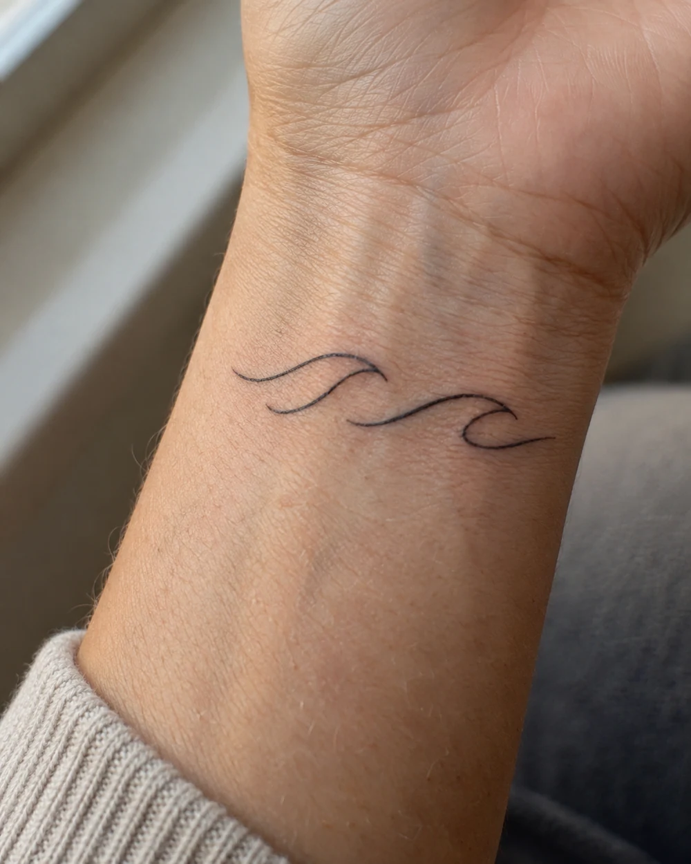 Minimal two-line black wave tattoo across a wrist