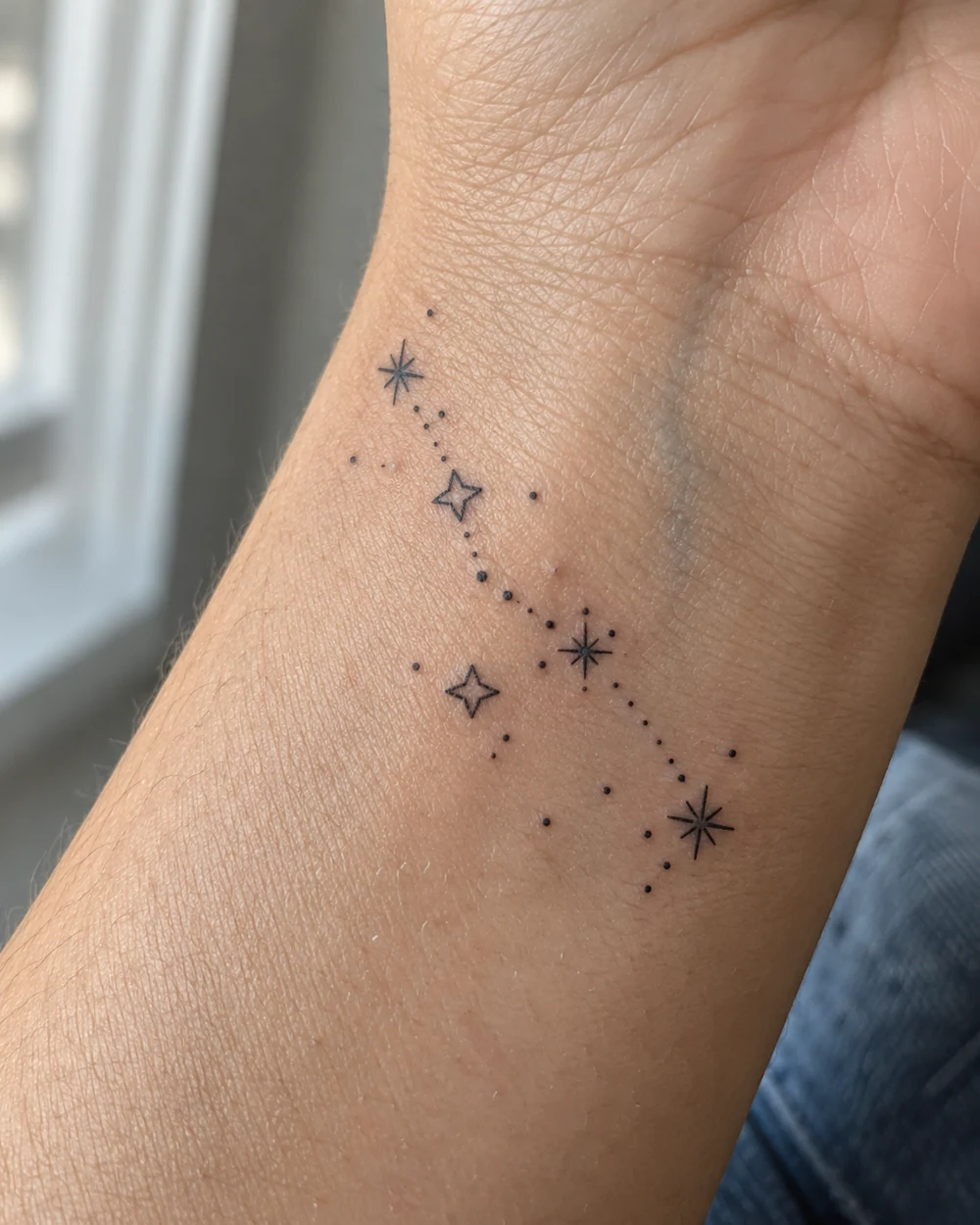 Tiny black constellation tattoo with outlined stars and dotted lines across a wrist